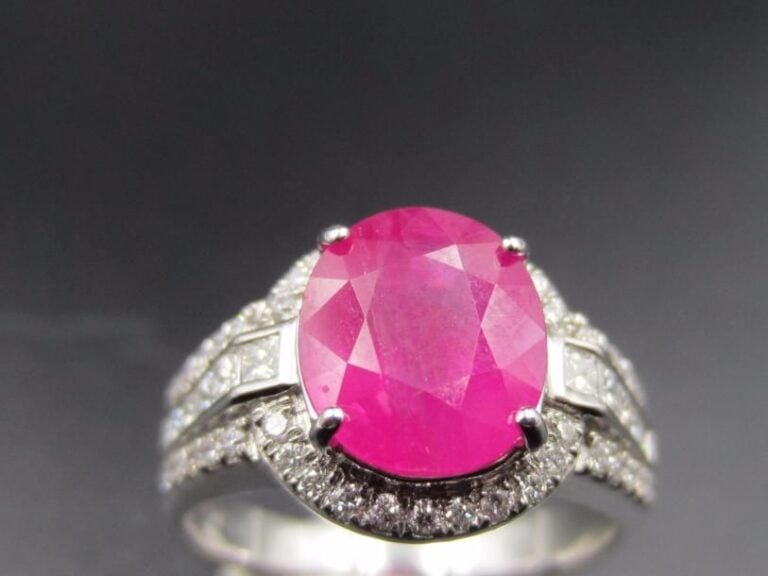 BAGUE en or gris (750 millièmes) serti d’un rubis de forme coussin, pesant 2,7 carats entouré de diamants taille brillant et épaulé de diamants princess