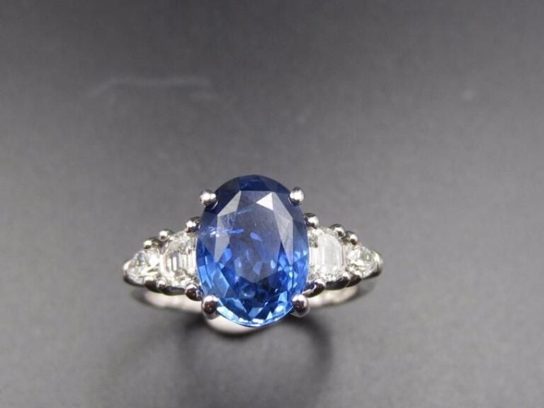 BAGUE en or gris (750 millièmes) serti d’un saphir de forme ovale, pesant 3,55 carats, épaulé de deux diamants demi-lune et deux diamants taillés en poir