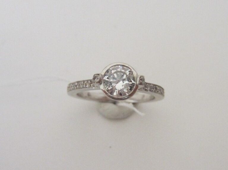 BAGUE en or gris (750 millièmes) surmonté d'un diamant taille brillant en serti clos, épaulé de petits diamant