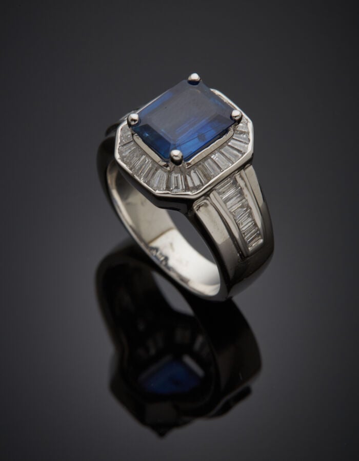 BAGUE en or gris (750‰) serti d'un saphir taillé à degrés, entouré et épaulé de…