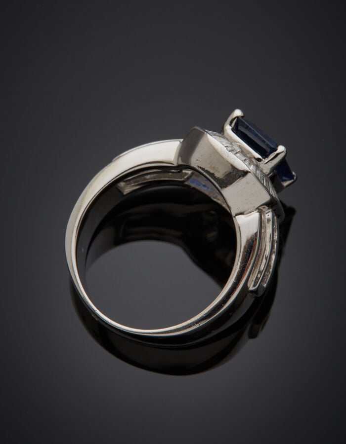 BAGUE en or gris (750‰) serti d'un saphir taillé à degrés, entouré et épaulé de…