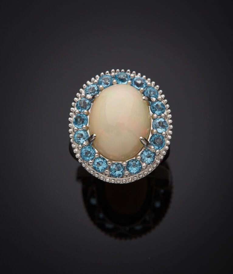 BAGUE en or gris (750‰) serti d'une opale cabochon, entourée de seize topazes b…