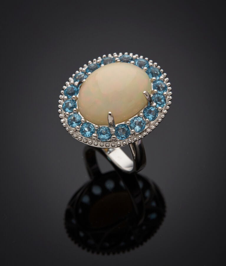 BAGUE en or gris (750‰) serti d'une opale cabochon, entourée de seize topazes b…