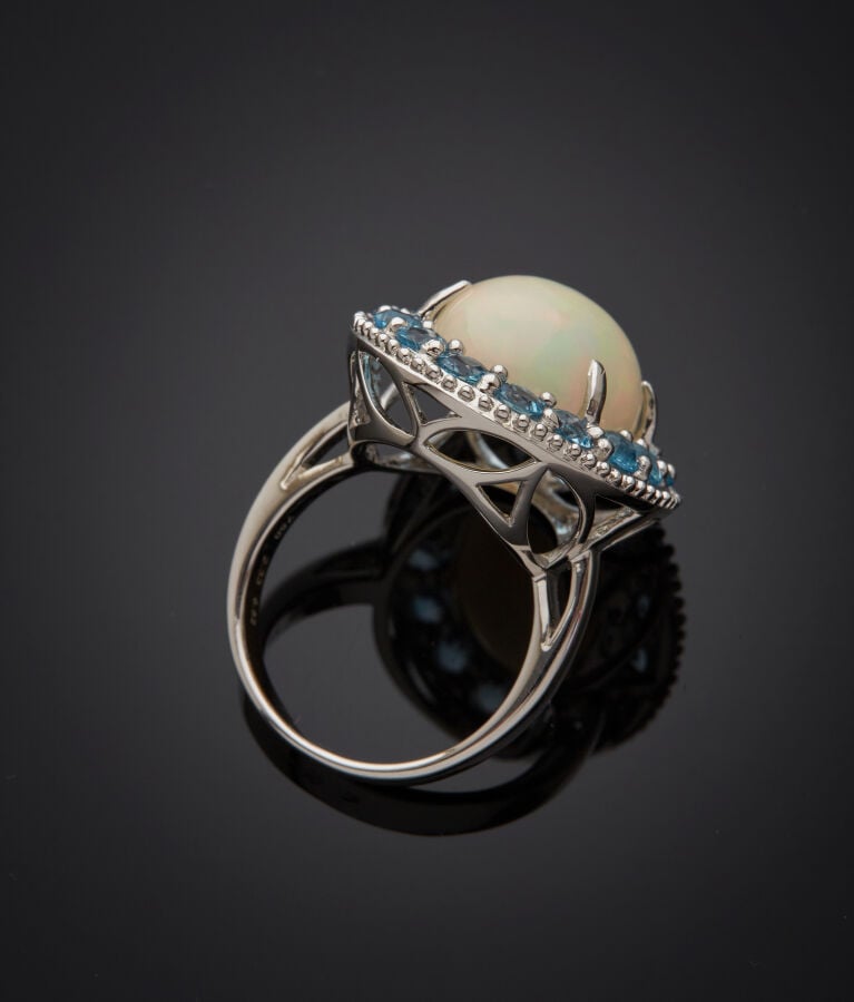 BAGUE en or gris (750‰) serti d'une opale cabochon, entourée de seize topazes b…