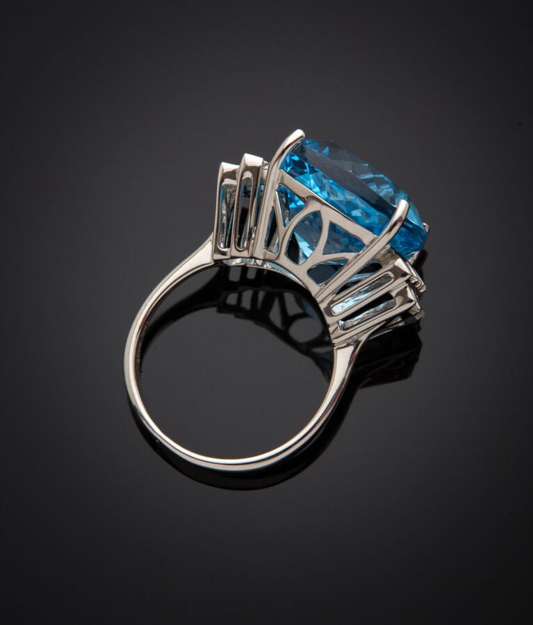 BAGUE en or gris (750‰) serti d'une topaze bleue taille coussin, épaulée de dia…