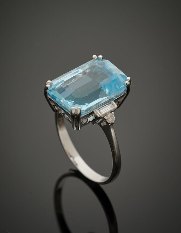 BAGUE en or gris (750‰) serti d'une topaze bleue taillée à degrés, épaulée de d…