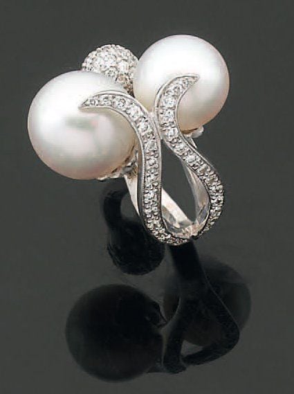 BAGUE en or gris ajouré serti de deux perles de culture blanches et de diamants taille brillant, à motif de volutes et boul