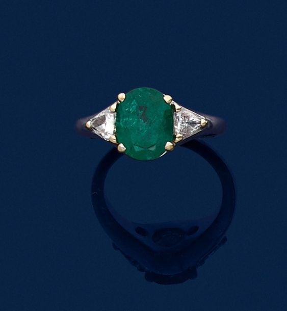 •BAGUE en or gris et or jaune (750‰) serti d'une émeraude ovale, épaulée de diamants troïda