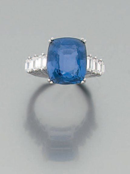 BAGUE en or gris serti d'un important saphir de forme coussin épaulé de trois diamants taille émeraude de chaque côt