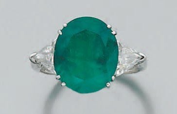BAGUE en or gris serti d'une émeraude de forme ovale épaulée de deux diamants troïda