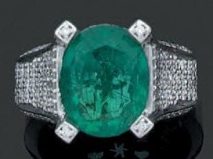 BAGUE en or gris serti d'une émeraude de forme ovale épaulée et entourée de pavages et alignements de diamants taille brillan