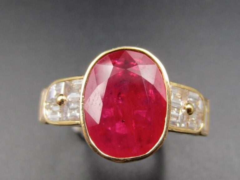 BAGUE en or jaune (750 millièmes) orné d’un rubis de forme coussin pesant 4,6 carats environ, en serti clos épaulé de dix diamants taille émeraude et baguettes              Doigt : 54        Poids brut : 6,9 g