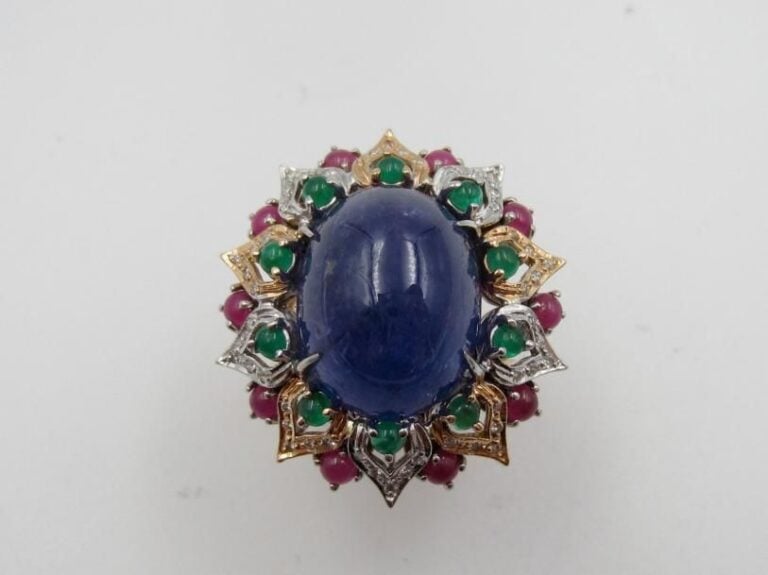 BAGUE en or jaune et or gris (585 millièmes) ajouré à motifs de pétales serti d‘une importante tanzanite cabochon de forme ovale entourée d’émeraudes cabochons et rubis             Doigt : 57        Poids brut : 16       2 g