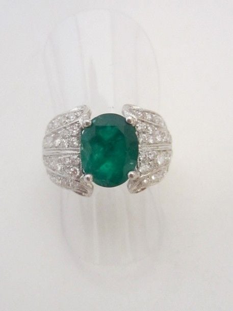 BAGUE en or platine (900 millièmes) finement ciselé serti d’une émeraude de forme ovale (égrisures) épaulée de lignes de diamants taille brillan