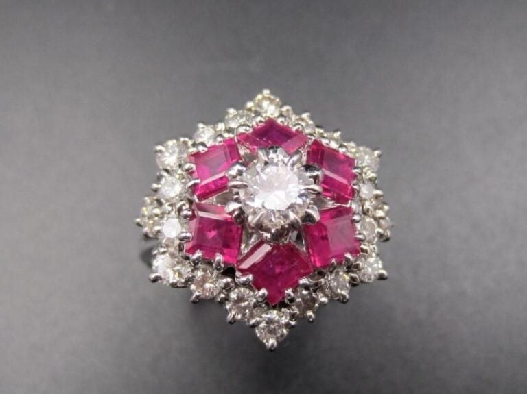 BAGUE « étoile » en or gris (750 millièmes) serti de diamants taille brillant dont un, au centre plus important, entouré de rubis calibrés        Travail français, vers 1970             Doigt : 54        Poids brut : 8,2 g