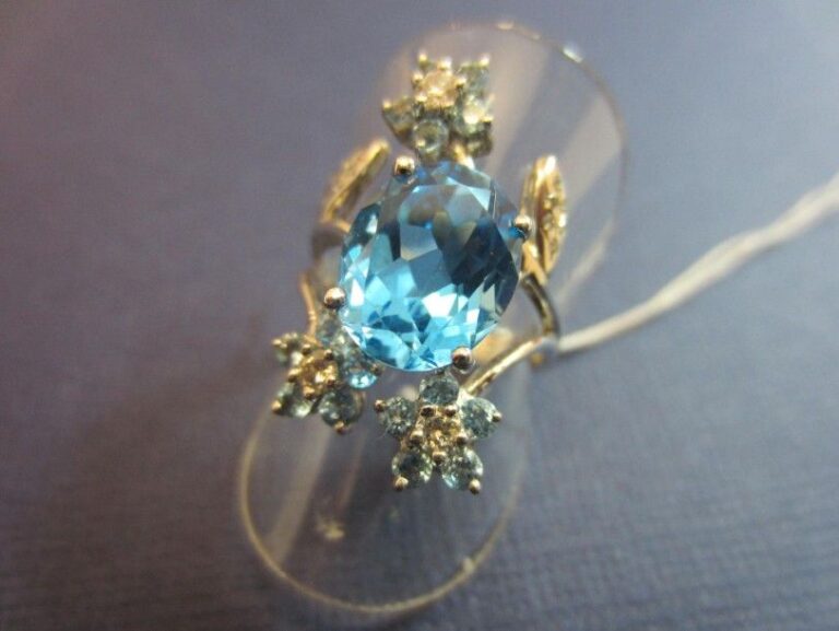 BAGUE «fleurettes» en or gris (750 millièmes) serti de topazes bleues, dont une au centre plus importante de forme ovale, entourée de diamants taille brillant et petites topazes bleue