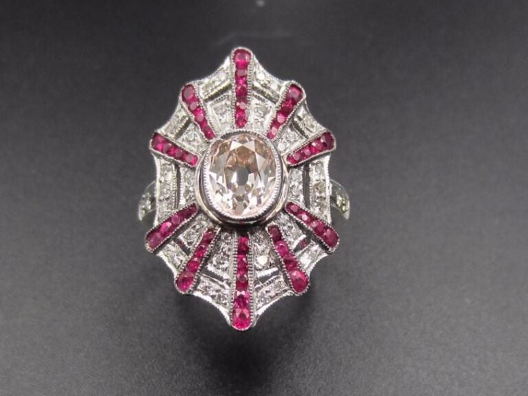 BAGUE « géométrique » en or gris (750 millièmes) serti d‘un diamant taille ancienne de forme ovale entouré de diamants taille brillant  alternés de rubis ronds, en chut