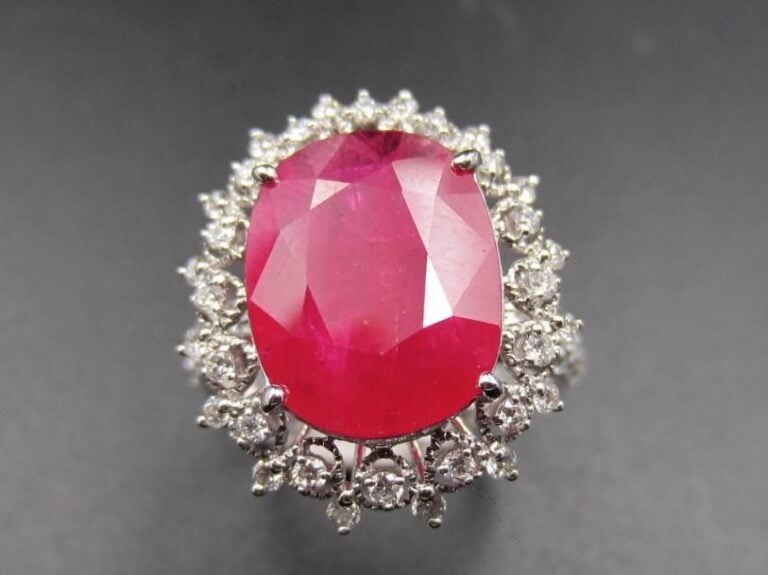 BAGUE « marguerite » en or gris (750 millièmes) ajouré à motifs de « dentelle » serti d’un rubis de forme coussin pesant 4,63 carats, entouré de diamants taille brillant             Doigt : 54        Poids brut : 5,1 g