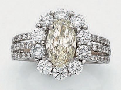 BAGUE «marguerite» en or gris (750 millièmes) ajouré, serti d'un diamant ovale, pesant 2 carats environ, entouré et épaulé de diamants taille brillan