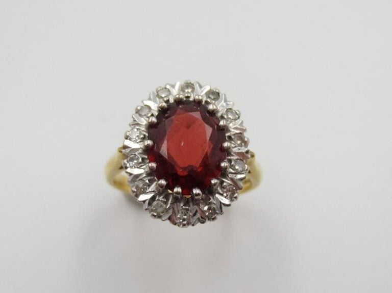 BAGUE « marguerite » en or jaune et or gris (750 millièmes) ciselé orné d’un grenat de forme ovale entouré de diamants taille 8      8             Doigt : 52        Poids brut : 4,8 g