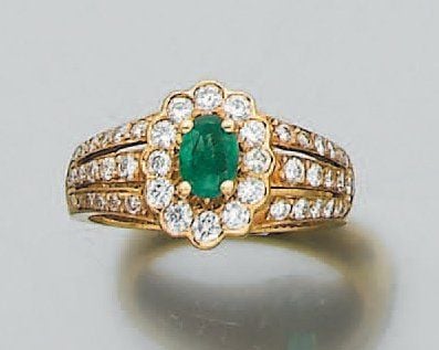 BAGUE « marguerite » en or jaune serti d'une émeraude de forme ovale épaulée et entourée de diamants de taille brillan