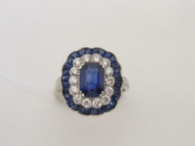 BAGUE «marguerite» en platine (950 millièmes) festonné, serti d'un saphir taillé à degrés, dans un double entourage de diamants taille brillant et saphirs calibré
