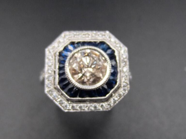 BAGUE octogonale en or gris (750 millièmes) serti de diamants taille brillant dont un, au centre, plus important pesant 1 carat environ, alternés de saphirs calibrés             Doigt : 53        Poids brut : 4,1 g