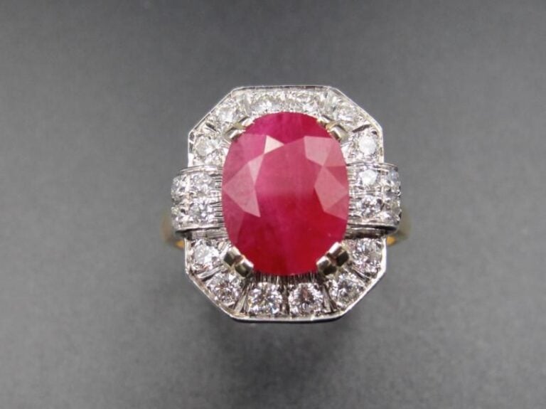 BAGUE octogonale en or jaune et or gris (750 millièmes) serti d’un rubis de forme ovale, pesant 3,39 carats, entouré et épaulé de diamants taille brillant             Doigt : 54        Poids brut : 7,8 g
