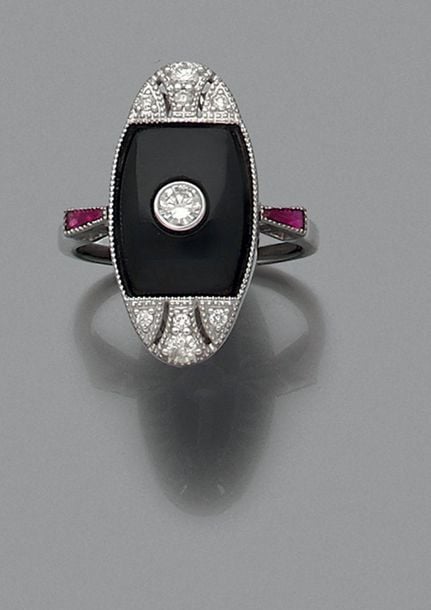 BAGUE ovale en or gris (750 millièmes) orné d’une plaque bombée en onyx, serti de diamants taille brillant dont un, au centre, plus important et épaulé de rubis calibré