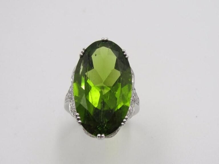 BAGUE ovale en or gris (750 millièmes) serti d’un important péridot pesant 19,4 carats, épaulé et entouré d’un motif juponné pavé de diamants taille brillan