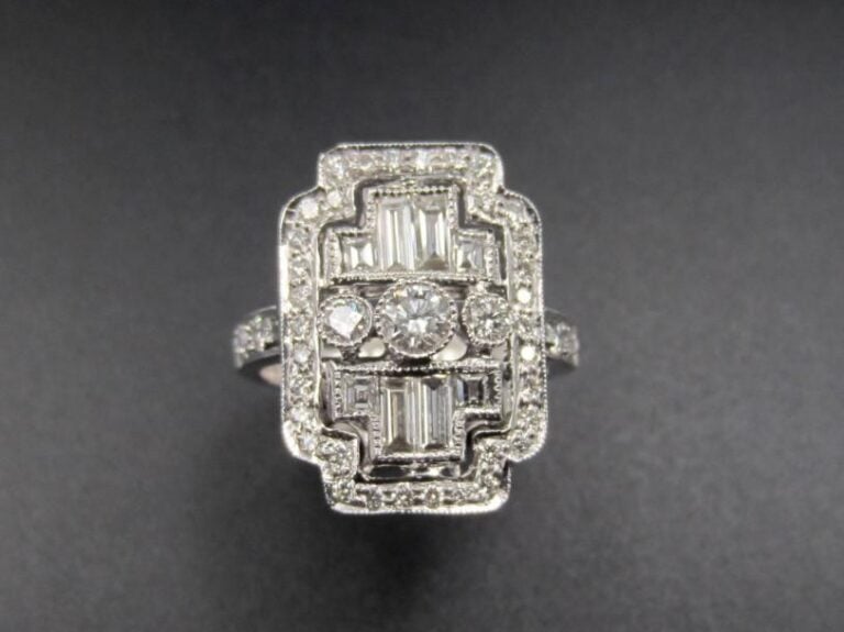 BAGUE « plaque » en or gris (750 millièmes) finement ajouré serti de diamants taille brillant dont trois, au centre, plus important soulignés de diamants baguettes et taillés à degrés             Doigt : 53        Poids brut : 7,5 g