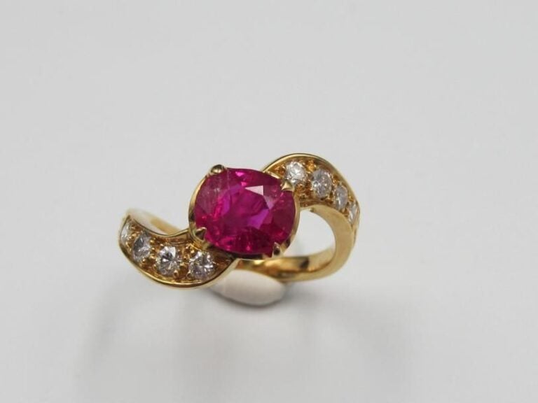 BAGUE «volutes» en or jaune (750 millièmes) serti d'un rubis de forme ovale épaulé huit diamants taille brillan