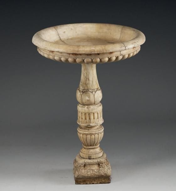Baignoire à oiseaux en forme de vasque en marbre blanc à décor de godrons; elle repose sur un fût à feuilles stylisées, cannelures rudentées, bagues et godrons; socle carré à cornes d'abondanc