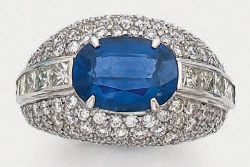 Belle BAGUE bombée en or gris (750 millièmes) serti d'un saphir de forme ovale, pesant 4,90 carats, épaulé de diamants taille princesse et pavages de diamants taille brillan