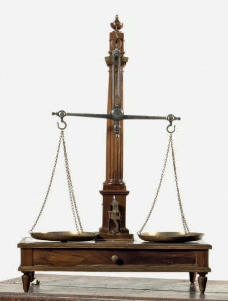 Belle balance de précision en noyer, placage de noyer, acier et laiton; le fléau soutenu par un système à vis supporté par une colonne fuselée à cannelures; la base est agrémentée de moulures en laiton, comporte un tiroir et repose sur des petits pieds fuselé