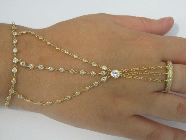 BIJOU DE MAIN composé d?un BRACELET reliant une BAGUE par des chaînettes, en or jaune (750 millièmes) serti de pierres blanches d?imitation