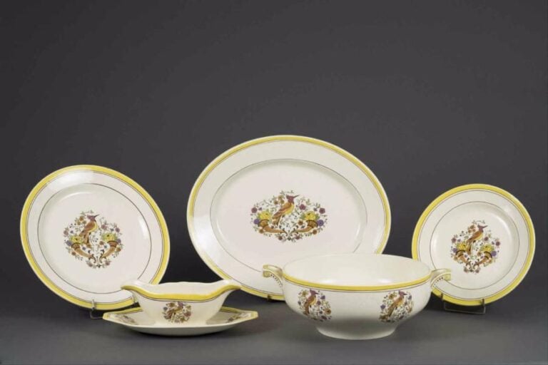 BOCH FRERES LA LOUVIERE Ensemble en faïence comprenant une saucière, un plat rond, un plat ovale, une coupe sur piédouche et une soupière à décor polychrome d'un oiseau dans un médaillon fleuri et cornes d'abondance, contours à filets marron et bandes jaune