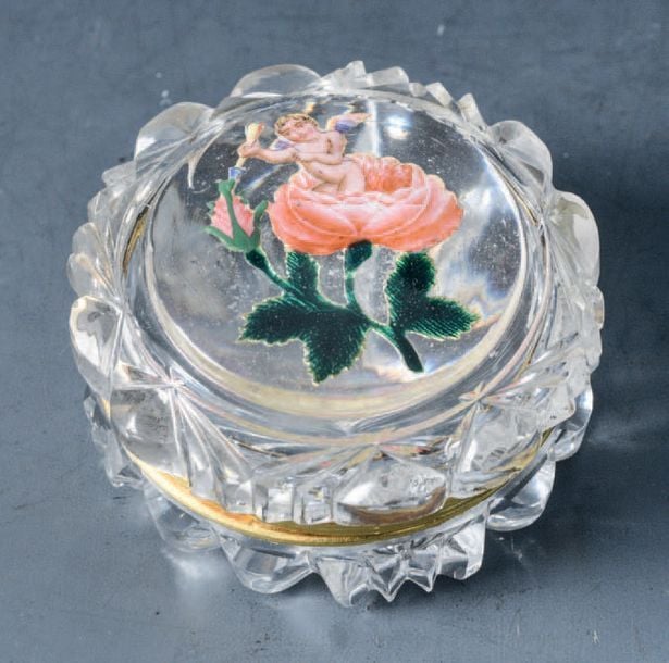 Boîte à mouches en cristal taillé, le couvercle orné d'un motif émaillé sur paillon d'or représentant un amour sortant d'une rose et tenant une flèche en main; monture en métal dor