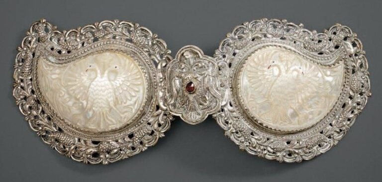 Boucle de ceinture Argent repoussé et ciselé et cabochon de verre rouge, cartouches de nacre avec traces de polychromie Grece, XIXe siecle Largeur: 27 cm Cette boucle de ceinture est centrée de deux aigles affrontés autour d'un cabochon de verre roug