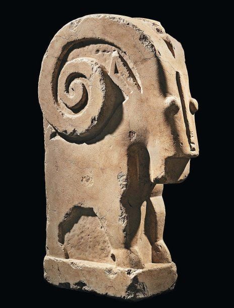 BOUQUETIN Grande statue de bouquetin en albâtre, au corps stylisé, debout sur une plateforme, la tête rectangulaire aux yeux globuleux, pourvue d'une barbe et coiffée de deux très grandes cornes enroulées en volutes autour de ses oreilles dressée
