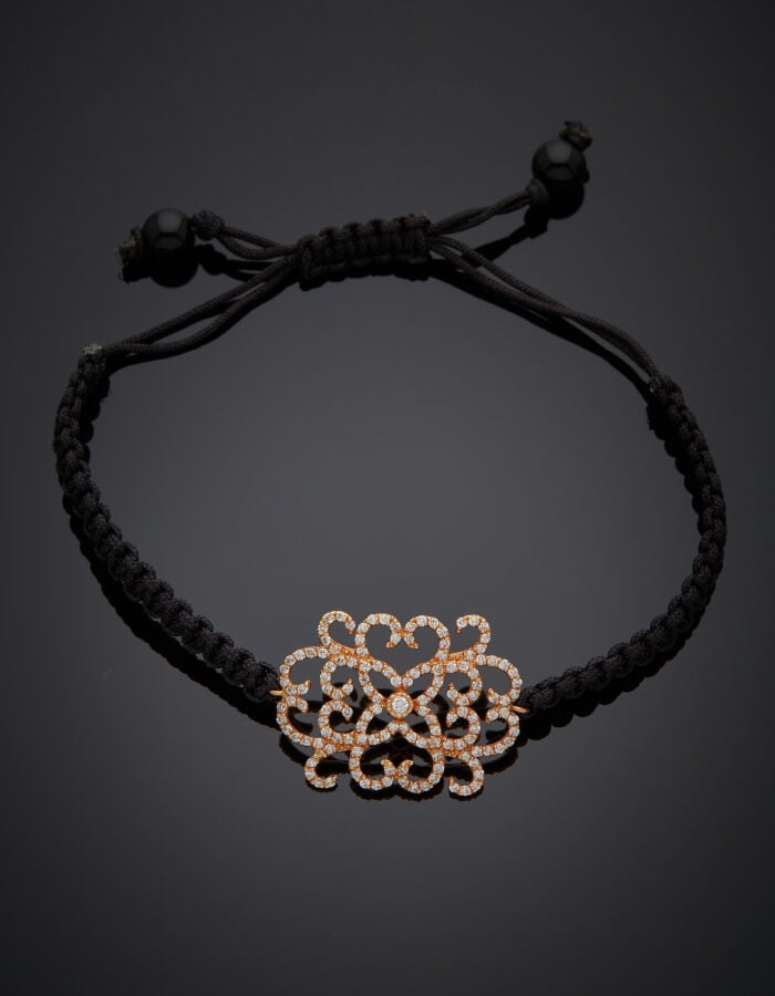 BRACELET "arabesques" composé d'un cordon noir tressé retenant un motif en or r…