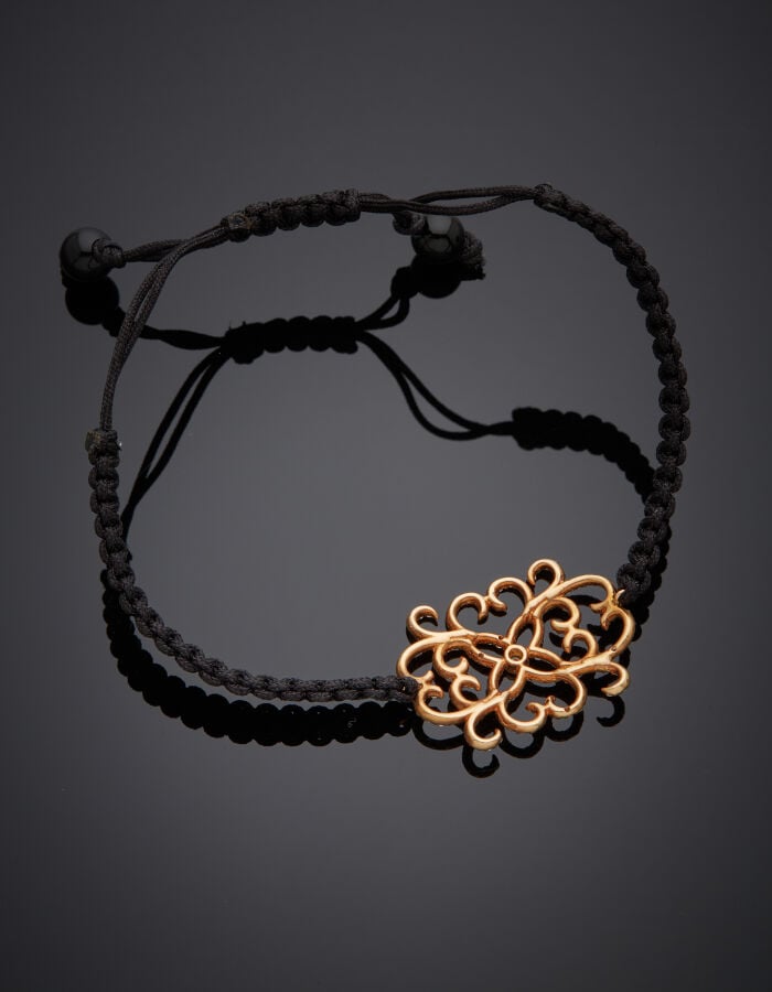 BRACELET "arabesques" composé d'un cordon noir tressé retenant un motif en or r…
