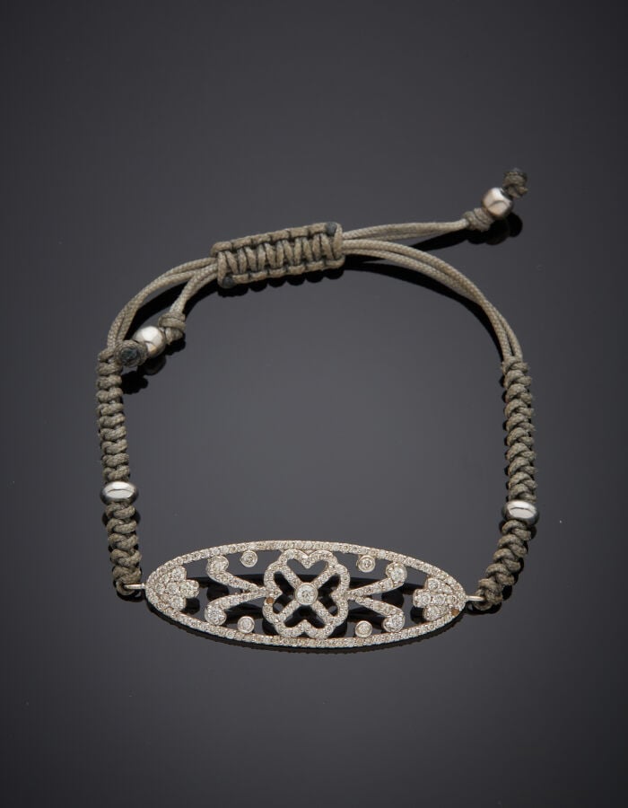 BRACELET composé d'un lien gris noué retenant un motif ajouré "fleur" en or gri…