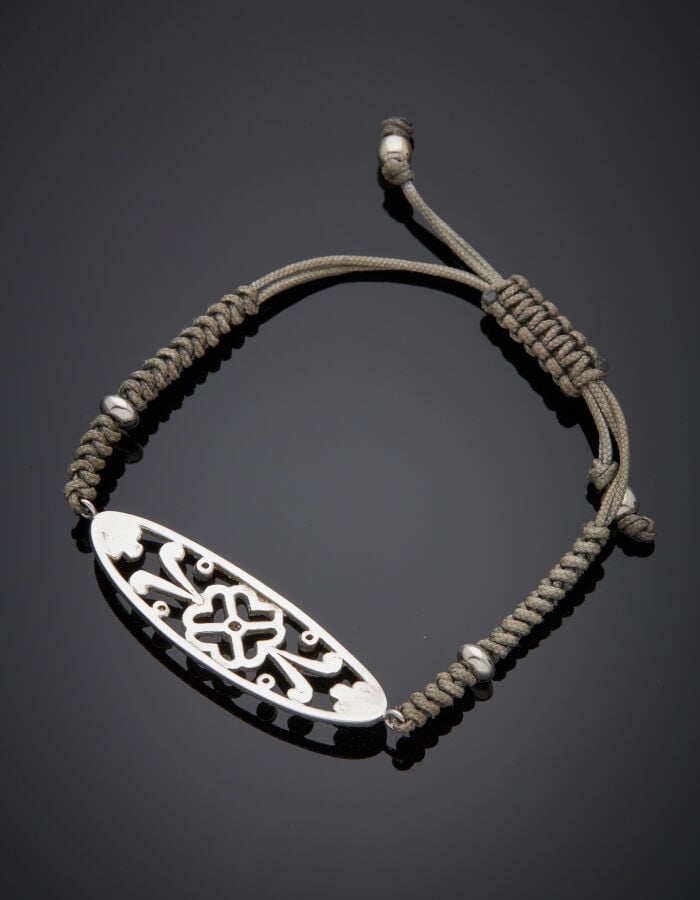 BRACELET composé d'un lien gris noué retenant un motif ajouré "fleur" en or gri…