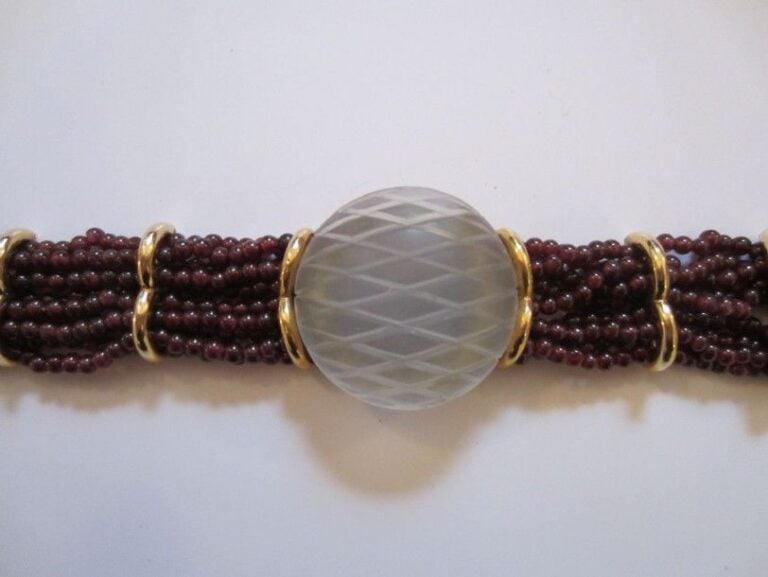 BRACELET en or jaune composé de rangs de perles de grenat surmontés au centre d'une importante pastille bombée en cristal de roche gravé de losanges, et retenus par des motifs "ponts" en or jaune; fermoir barrette en vermeil cisel
