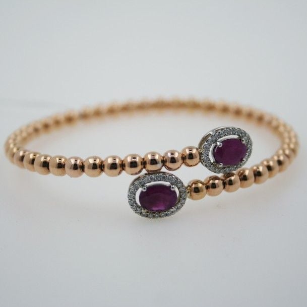 BRACELET légèrement flexible, ouvert en or jaune et or gris (750 millièmes) composé d'un alignement de boules d'or, terminé par deux rubis de forme ovale entouré de diamants taille brillan