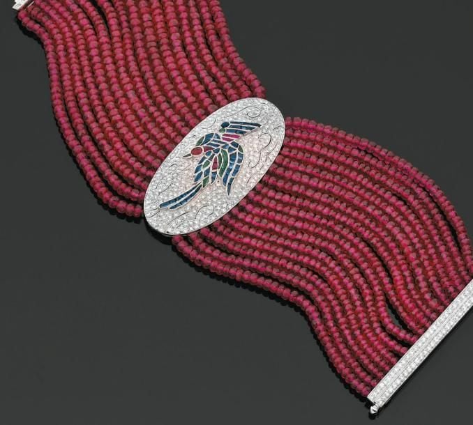 BRACELET «manchette» composé de seize rangs de perles de rubis facettés retenant une plaque ovale en or gris finement ajouré, à motif d'«oiseau du paradis» pavé de diamants et rehaussé de saphirs, émeraudes et rubis, calibrés, facetté et suifé