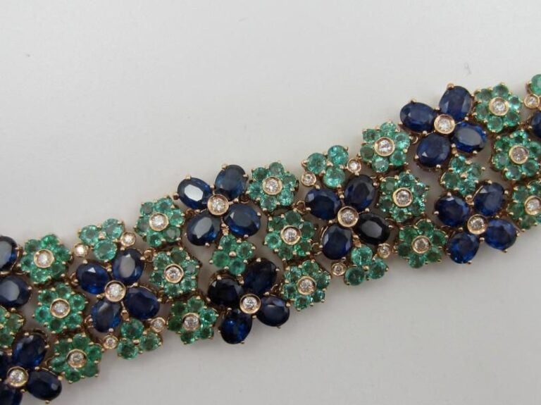 BRACELET manchette en or jaune (585 millièmes) 14 carats ajouré à motifs de fleurettes serties d’émeraudes de forme rondes et saphirs ovales alternés de diamants taille brillant             Long        : 18,5 cm        Poids brut : 45,6 g