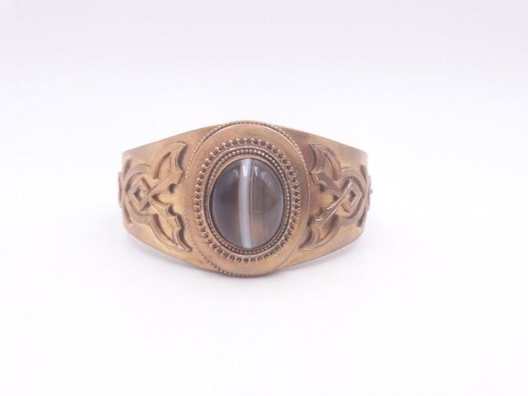 BRACELET MANCHETTE rigide ouvrant en métal doré, perlé et ciselé, centré d’un important cabochon d’ony