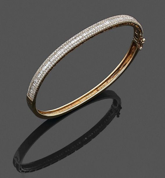 •BRACELET rigide ouvrant en or jaune (750‰) serti d'un alignement de diamants baguettes souligné de diamants taille brillan